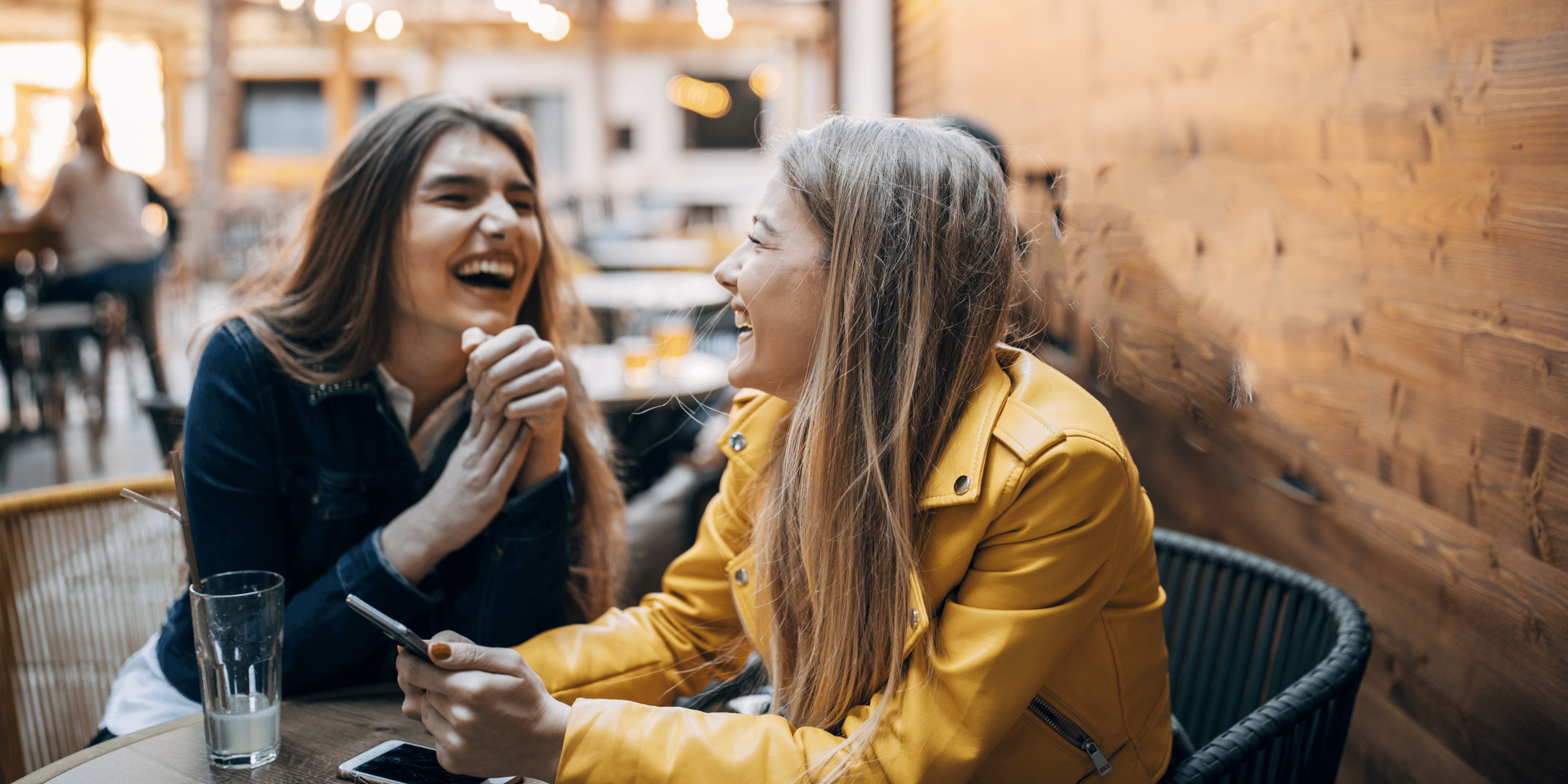 Image of two friends, young women, laughing and catching up at a cafe